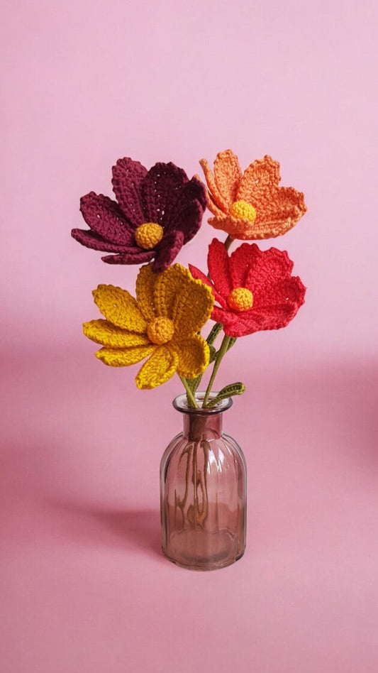 Un ensemble de fleurs de cosmos faite au crochet. Chaque fleur présente des détails délicats, avec des textures bien définies et des couleurs vives comme le rouge, le jaune et le orange